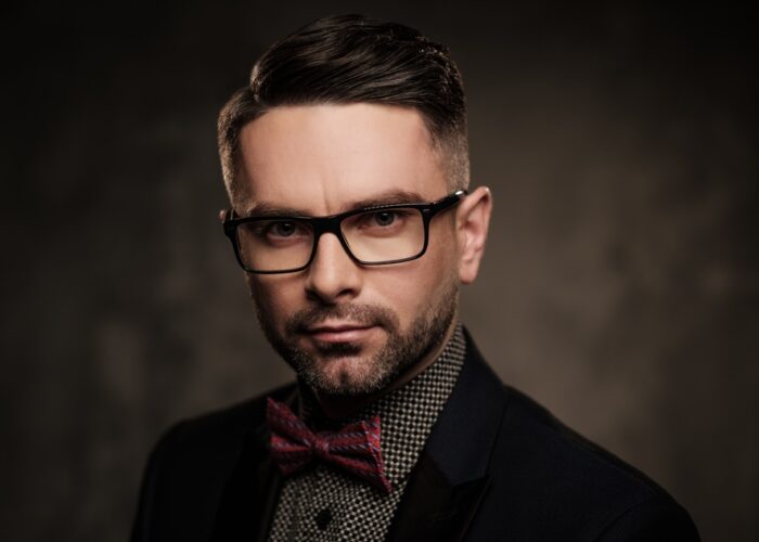 Well-groomed stylish young man with bow tie posing on dark background.
